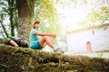 Cheerful smiling young female backpacker sitting on the old stone castle fance and enjoying a rest time on the Way of Camino de Sa