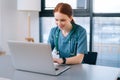 Cheerful smiling young female doctor in blue green medical uniform typing on laptop computer looking on screen Royalty Free Stock Photo