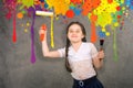 Cheerful smiling young little girl the child draws on the background wall colored paints making a creative repairs.