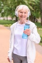 cheerful sportswoman with bottle of water and headphones standing in park