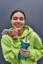 cheerful sportswoman in hoodie holding bottle