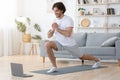 Cheerful sporty guy exercising at home, using laptop