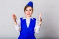 A cheerful stewardess in a blue cap looks at the camera and makes gestures with her hands