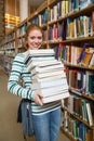 Cheerful student holding heavy pile of books standing in library Royalty Free Stock Photo