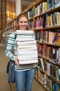 Cheerful student holding huge pile of books standing in library Royalty Free Stock Photo