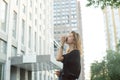 Cheerful stylish businesswoman drinking coffee outside on urban background. Attractive young woman enjoying coffee outdoors on the Royalty Free Stock Photo