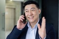 Cheerful and successful asian businessman working inside office at workplace, boss talking smiling on phone, man in Royalty Free Stock Photo