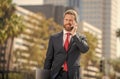 cheerful successful businessman in suit talking on phone standing outdoor, mobile technology Royalty Free Stock Photo