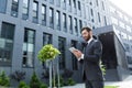 Cheerful and successful businessman works outdoors near the office holds a tablet, smiles reads good news Royalty Free Stock Photo