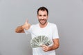 Cheerful successful young man holding money and showing thumbs up Royalty Free Stock Photo