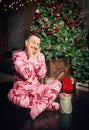 Cheerful surprised funny man in pink sleepwear sitting near decorated fir tree and Christmas present Royalty Free Stock Photo