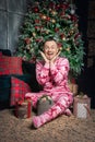 Cheerful surprised funny man in pink sleepwear sitting near decorated fir tree and Christmas present Royalty Free Stock Photo