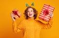 Cheerful surprised woman laughs with her mouth open holds a Christmas gifts on a colored yellow background