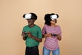 Cheerful surprised young black man and lady with big belly, VR glasses play online game with joysticks Royalty Free Stock Photo