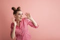 Cheerful surprised young woman with two bun hairstyles looks to the side on a pink background. Adults are like children. Pink mood