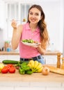 Cheerful svelte young woman eating vegetable salad in home kitchen