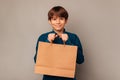 Cheerful teen boy is holding tight a clean shopping bag with copy space.