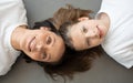 Cheerful teen european girl and millennial woman lie on gray floor background, enjoy workout together Royalty Free Stock Photo