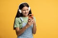 Cheerful teen school girl looking for modern song in smartphone app, listening to music in earphones