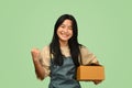 Cheerful teenage Asian girl holding parcel box on green background. Post, package, shipping and delivery concept