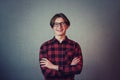 Cheerful teenage guy hipster, wearing casual red shirt and glasses, keeps hands folded looking joyful to camera isolated on grey Royalty Free Stock Photo