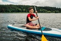 Cheerful teenager sitting on a sap surf and rowing with an oar Royalty Free Stock Photo
