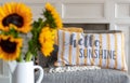 Cheerful throw pillow that says hello sunshine with sunflowers in the blurred foreground