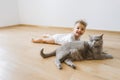 cheerful toddler boy and grey british shorthair cat lying on floor together