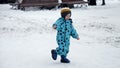 Cheerful toddler boy in snowboots and ski suit happily running on street covered with snow. Cheerful baby, kids playing at winter Royalty Free Stock Photo