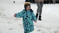 Cheerful toddler boy in snowboots and ski suit happily running on street covered with snow. Cheerful baby, kids playing at winter.