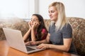 Cheerful toothy smiling happy mother and her little curious daughter are lying on a floor at home and usinf a laptop for