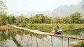 Cheerful Tourist crossing bamboo bridge motorbike, limestone view, laos