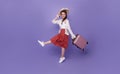 Cheerful traveler tourist woman in summer clothes hat jumping running hold suitcase isolated on purple background