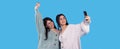 Cheerful twin girls making selfie isolated on blue background one of them raised her right hand up and smiling. Royalty Free Stock Photo