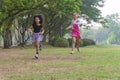 Cheerful two little kids having fun while running through grassy field with tree and racing against each other. Cute girl enjoying