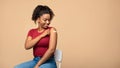 Cheerful vaccinated Afro woman showing plaster on her shoulder after immunization against covid over beige background