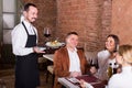 Cheerful waiter placing order in front of guests Royalty Free Stock Photo