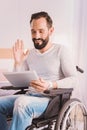 Cheerful wheelchaired man uisng a tablet for communication