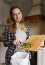 Cheerful white woman composting organic food waste at home. Portait of responsible housewife recycling leftovers in a bokashi bin
