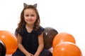 Cheerful winsome adorable little girl in black carnival dress and hoop with cat ears sitting on a white surface with bi colored Royalty Free Stock Photo