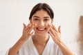 Cheerful Woman Applying Facial Cream Moisturizing Skin Posing In Bathroom Royalty Free Stock Photo