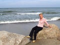 The cheerful woman of average years sits on a boulder. Coast of the Baltic Sea