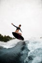 Cheerful woman in black wetsuit effectively jumps on surfboard on wave Royalty Free Stock Photo