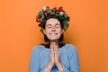 Cheerful woman in Christmas wreath hands folded in prayer beg about something good, dressed in winter blue sweater, make wish