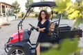 Cheerful woman with curly hair in black dress holding in hands a laptope, poses near vehicle and smiling Royalty Free Stock Photo