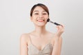 Cheerful woman is doing make up on her face using brush. Beauty routine on white background Royalty Free Stock Photo