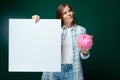 Cheerful woman dressed in a checkered shirt talks about savings using a board and holds a piggy bank Royalty Free Stock Photo