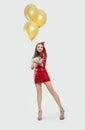 Cheerful woman fashion model in red party dress with little pig and yellow balloons on white background Royalty Free Stock Photo