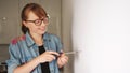 cheerful woman with glasses putting a screw into the wall for hanging a frame, medium closeup kitchen
