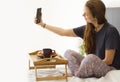 Cheerful Woman having breakfast in bed. Tea and pancakes with strawberry. Asian caucasian woman blogger smiling and making selfie Royalty Free Stock Photo